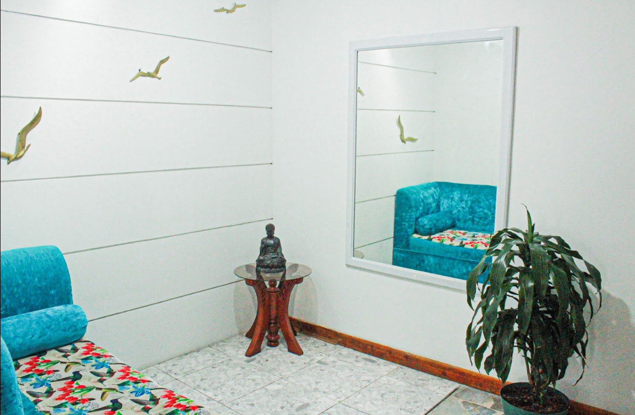 Sala de El Cable Hostal con sofá turquesa, espejo y planta